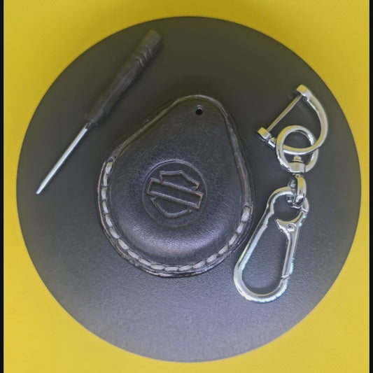 Video of a gray premium leather key fob cover for Harley Davidson motorcycles with light gray stitching rotating on a display turntable with a stainless steel lobster clasp keychain and screwdriver.