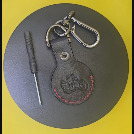 Black veg-tanned leather apple airtag with red stitching on a keychain rotating on a display pedestal.