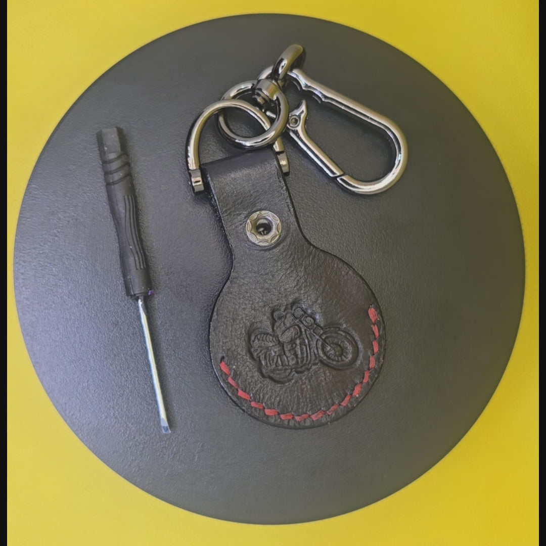 Black veg-tanned leather apple airtag with red stitching on a keychain rotating on a display pedestal.