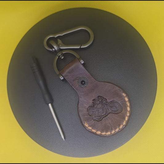 Video of a brown vegetable tanned leather Apple Airtag holder with motorcycle stamped into it on a keychain clasp turning on a display pedestal.