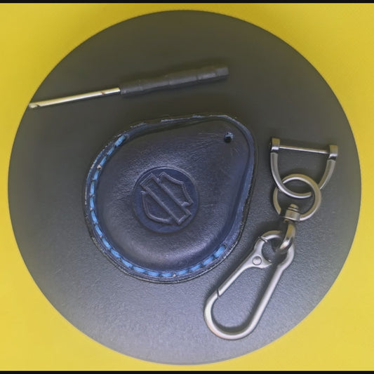 Video of a navy blue premium leather key fob cover for Harley Davidson motorcycles with blue stitching rotating on a display turntable with a stainless steel lobster clasp keychain and screwdriver.