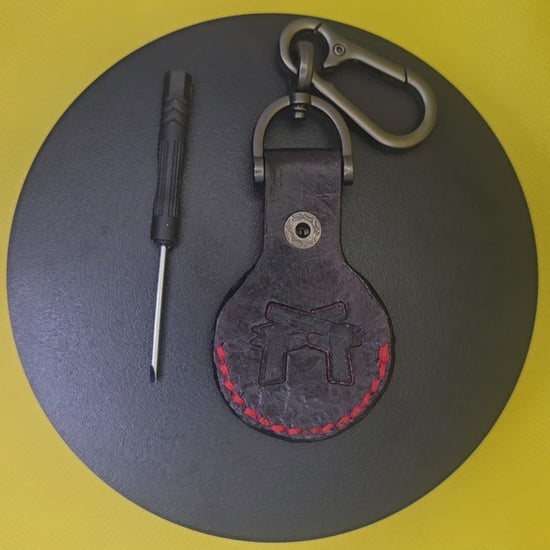 Black vegetable tanned apple airtag case with 2 guns stamped and red stitching, rotating on a display turntable.