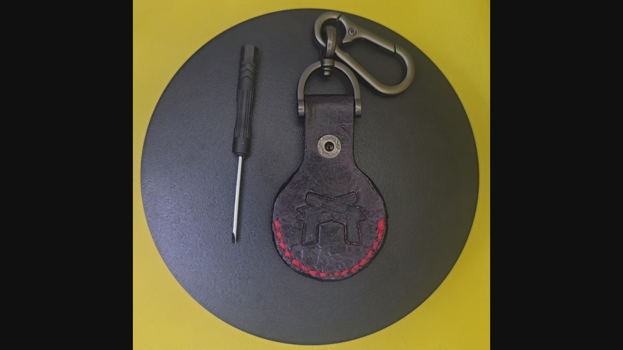 Black vegetable tanned apple airtag case with 2 guns stamped and red stitching, rotating on a display turntable.