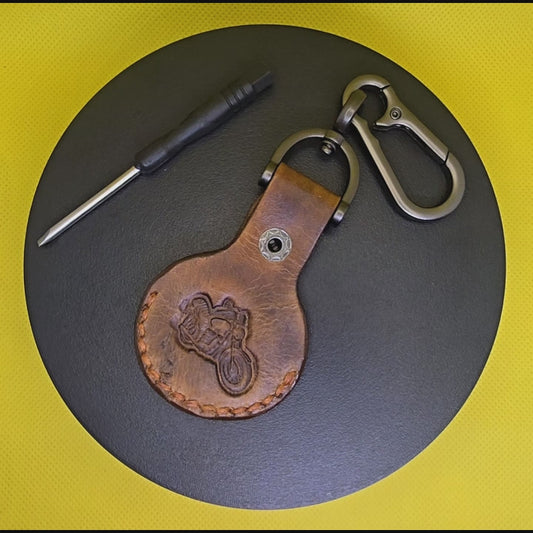 Video of a brown colored vegetable tanned leather Apple Airtag holder with a motorcycle stamped into it on a lobster clasp keychain turning on a display pedestal.