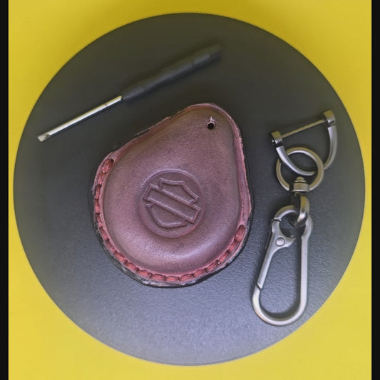 Video of a mahogany veg-tanned leather key fob case for Harley Davidson motorcycles rotating on a turntable with the included solid stainless steel lobster clasp keychain and screwdriver.