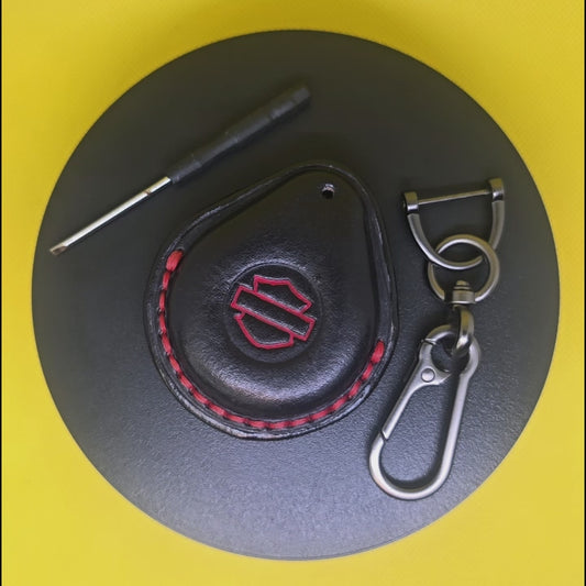 Video of a black and red Vegetable tanned leather key fob case for Harley Davidson motorcycles with red stitching and logo rotating on a turntable with the included stainless steel keychain and screwdriver.