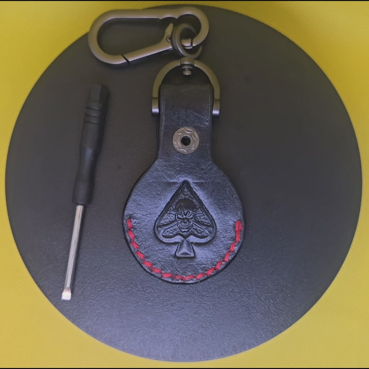 Black full-grain leather apple airtag pouch for apple air tags with red stitching and a spade with skull and crossbones stamped into the leather.
