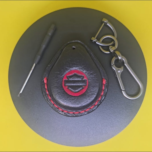 Video of a black and red Vegetable tanned leather key fob case for Harley Davidson motorcycles with red stitching rotating on a pedestal with the included stainless steel keychain and screwdriver.