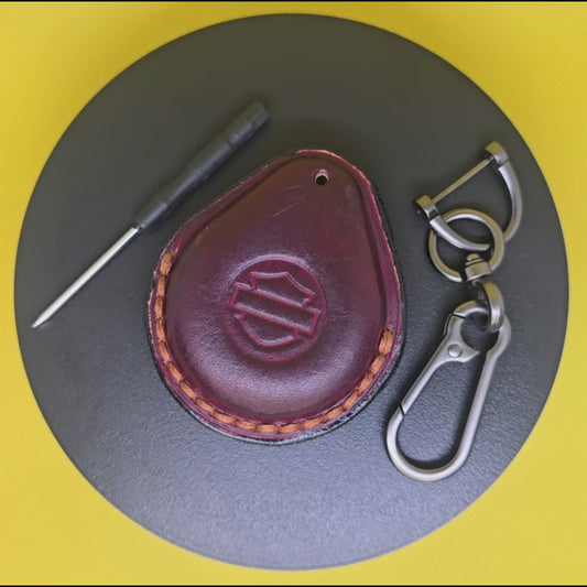 Video of a burgundy Veg-tanned leather key fob case for Harley Davidson motorcycles rotating on a turntable with the included solid stainless steel lobster clasp keychain and screwdriver.