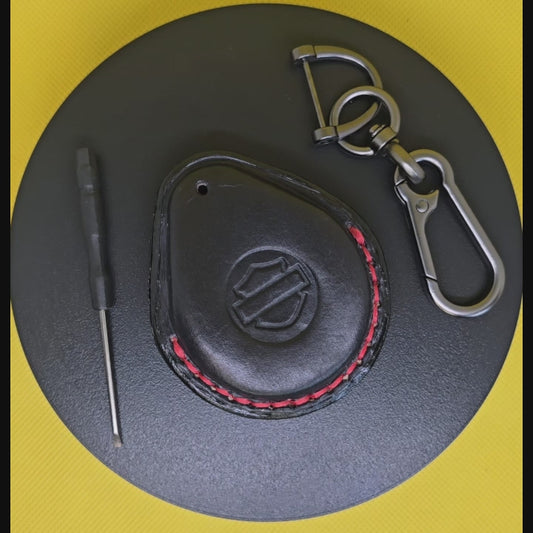 Video of a black Vegetable tanned leather key fob case for Harley Davidson motorcycles with red stitching rotating on a pedestal with included stainless steel keychain and screwdriver.